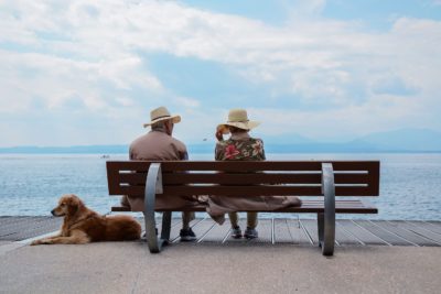 An elderly couple and their golden retriever sit by the lake shore.